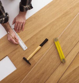 Carpenter installing a wooden flooring and measuring with a precision ruler, top view
