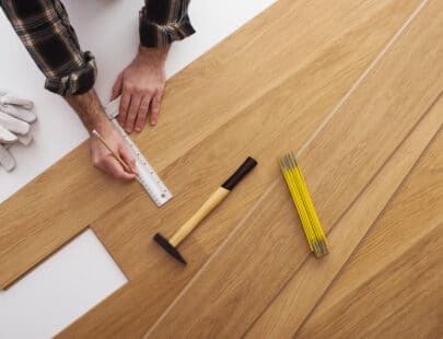 Carpenter installing a wooden flooring and measuring with a precision ruler, top view