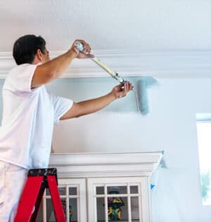 A housepainter stands on a ladder to paint the walls inside a residential home.  rr