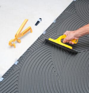 Spreading wet mortar before applying tiles on bathroom floor.