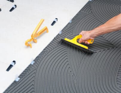 Plattsättare Spreading wet mortar before applying tiles on bathroom floor.
