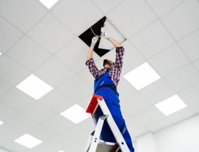 Full Length Portrait Of Electrician On Stepladder Installs Lighting To The Ceiling In Office