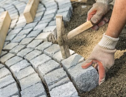 A workman's gloved hands use a hammer to place stone pavers Laying paving stone, just hands in gloves and a hammer in action, hammering on the paving stones.