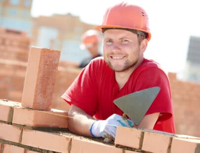 construction worker. Portrait of mason bricklayer installing red brick with trowel putty knife outdoors
